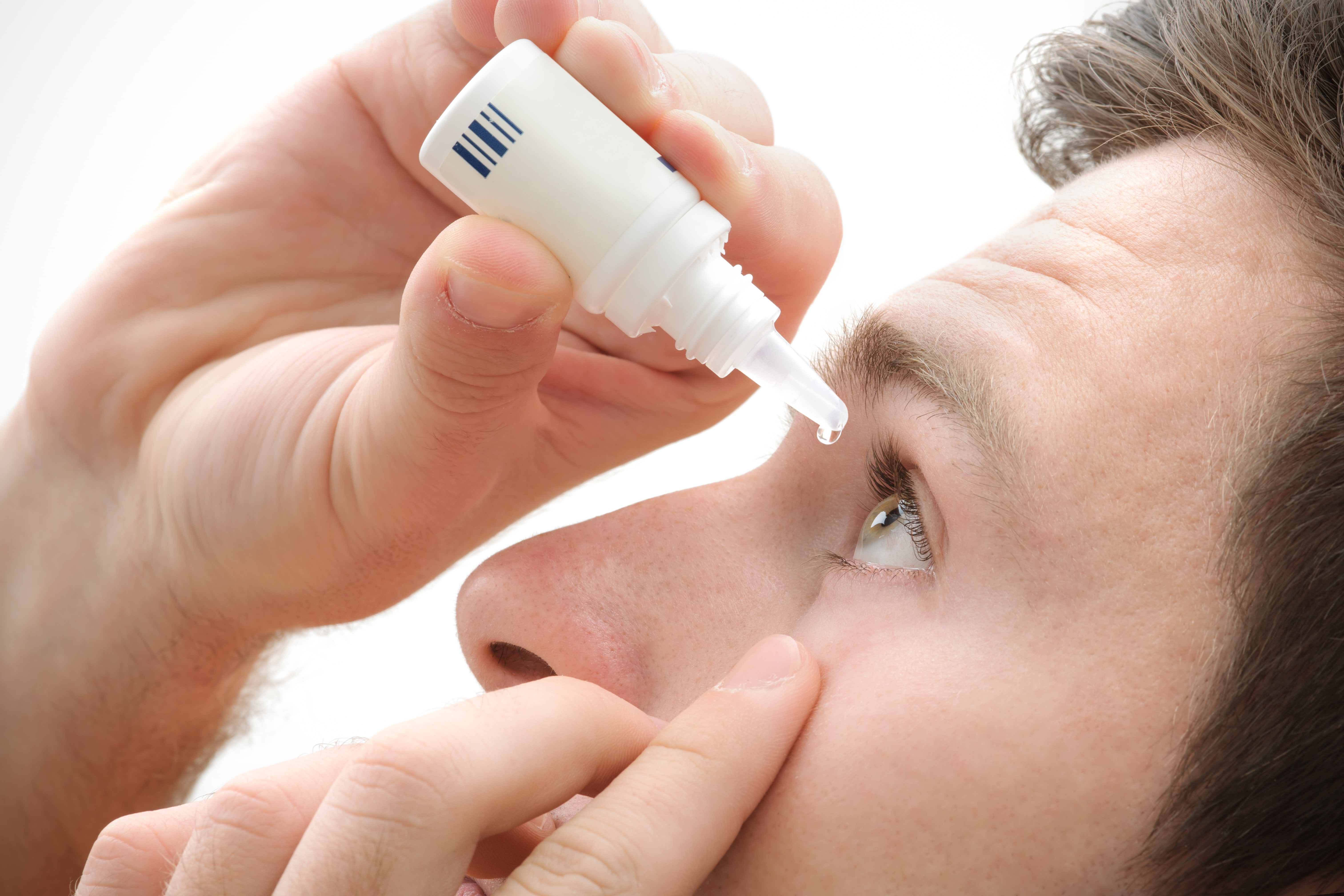 Guy using his finger to hold his eye open while administering eye drops