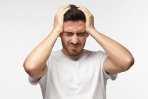 Man with a headache holding his head with both hands and a pained expression on his face